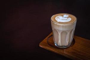 een glas latte art op een houten plaat met donkere achtergrond
