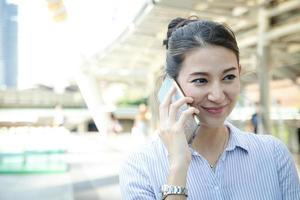 een mooi western vrouw toepassingen haar smartphone naar praten buitenshuis. ze glimlacht gelukkig. technologie, mobiel telefoon sollicitatie. bedrijf concept, werk of communicatie. met kopiëren ruimte foto