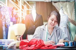 jong vrouw ondernemers de eigenaar van een klein kleding op te slaan is zittend Aan een mode ontwerp Aan de bureau met naaien apparatuur. opstarten bedrijf idee foto