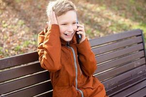 een emotioneel jongen is pratend Aan de telefoon Holding zijn hoofd en lachend foto