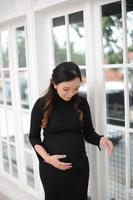 een zwanger vrouw vervelend een zwart jurk in voorkant van een glas deur foto