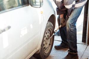 monteur veranderen een auto band in een werkplaats Aan een auto gebruik makend van een elektrisch boren naar losmaken de bouten foto