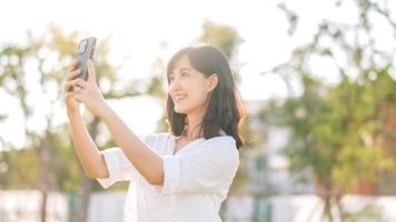 portret mooi jong Aziatisch vrouw met slim mobiel telefoon in de omgeving van buitenshuis natuur visie in een zonnig zomer dag foto