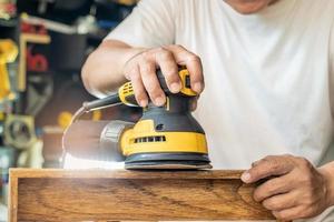 timmerman gebruikt excentrische schuurmachine of palmschuurmachine polijst hout in de werkplaats, doe-het-zelfmaker en houtbewerkingsconcept. selectieve focus foto