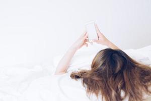 bijgesneden schot visie van Aziatisch vrouw aan het liegen Aan bed en gebruik makend van haar slim telefoon. conceptuele van vrouw levensstijl. foto