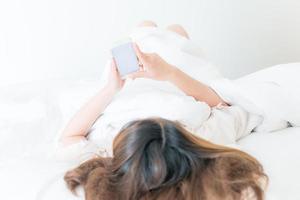 Aziatisch vrouw aan het liegen Aan bed en gebruik makend van haar slim telefoon. conceptuele schot van vrouw terwijl spelen telefoon. foto