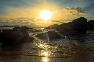 kleurrijk zonsondergang Bij strand met boom en rotsen foto