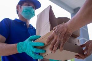 postbode draagt een masker en handschoenen, levering voedsel naar de huis van de online koper. blijven Bij huis verminderen de verspreiding van de covid-19 virus. de afzender heeft een onderhoud naar leveren producten of voedsel snel foto