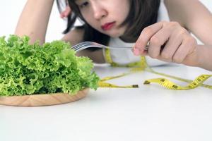 Aziatisch Dames zijn moe van aan het eten groenten gebruik makend van een vork van sla in de gerecht. gezond voedsel en eetpatroon concept foto