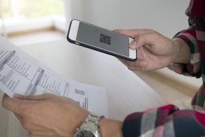 een Mens toepassingen een smartphone naar scannen de qr code naar betalen maandelijks credit kaart rekeningen na ontvangen een factuur verzonden naar huis. online Bill betaling concept foto