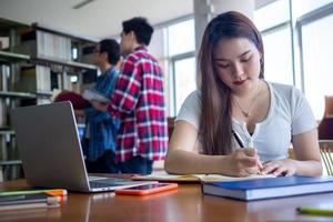 jong Aziatisch studenten in gewoontjes slijtage Doen huiswerk en gebruik een technologie laptop in de Universiteit bibliotheek. de studenten zijn zoeken voor kennis en zijn voorbereidingen treffen voor de examen. foto