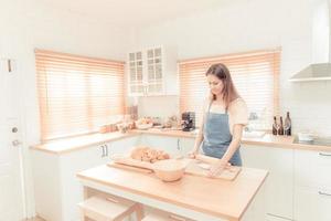 jong vrouw werk met houten rol pin maken zoet taart of gebakje deeg in keuken, gelukkig millennial vrouw liefhebbend Koken. warm toon. foto