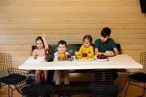 vier kinderen eten fruit in houten land huis Aan weekend. foto