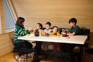 moeder met vier kinderen eten fruit in houten land huis Aan weekend. foto