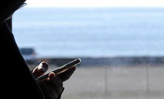 Mens Aan een trein op reis langs de kust spelen Aan zijn smartphone foto