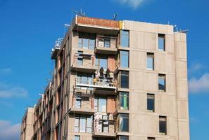 geschorst platform, bouw wieg hangende Aan gebouw. installatie en reparatie werk. gebouw gevels bouw werken. facade van hoogbouw gebouw onder bouw, afwerking werken foto