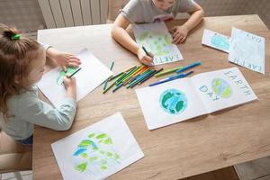 kinderen trek de planeet aarde met potloden en viltstift pennen Aan album lakens voor aarde dag Bij hun huis tafel. de concept van beschermen de omgeving, vrede Aan aarde. foto