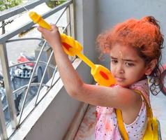 zoet weinig Indisch meisje spelen kleuren Aan holi festival, Holding pichakaree vol van kleuren, holi festival vieringen in Delhi, Indië foto