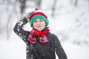 grappig weinig jongen in winter kleren wandelingen gedurende een sneeuwval. winter buitenshuis activiteiten voor kinderen. een schattig kind in een warm hoed verheugt zich Bij de eerste sneeuw. foto