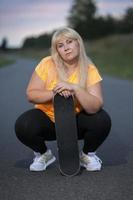 portret van een mollig Europese vrouw in een sport- tank top met een skateboard. foto