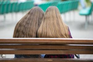 twee meisjes met lang haar- zijn zittend Aan een bank. terug visie. foto