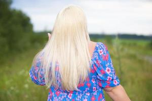 een mooi plus grootte meisje met wit haar- in een zomer bloem jurk staat met haar terug naar de camera. foto