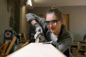 aantrekkelijk vrouw timmerman gebruik makend van sommige macht gereedschap voor haar werk in een hout winkel foto