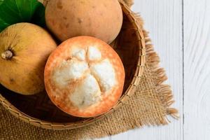 top visie van vers santol fruit Aan bamboe mand en Aan wit hout achtergrond, foto