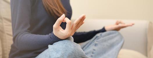 dichtbij omhoog handen van kalmte houding Aziatisch jong vrouw, meisje praktijk zitten, mediteren in lotus positie Aan sofa Bij huis, meditatie, oefening voor welzijn, gezond zorg. ontspanning, vrije tijd mensen. foto