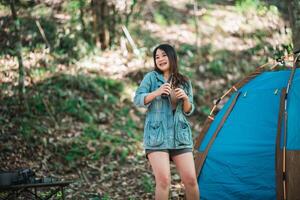 jong vrouw juichen en drinken drank voorkant van camping tent foto