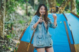 jong vrouw juichen en drinken drank voorkant van camping tent foto