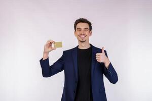 portret van jong glimlachen knap zakenman tonen credit kaart en duim omhoog geïsoleerd over- wit achtergrond foto