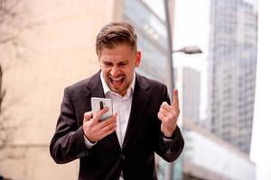 een jong vent in een bedrijf pak schreeuwt Bij de gesprekspartner Aan de telefoon foto