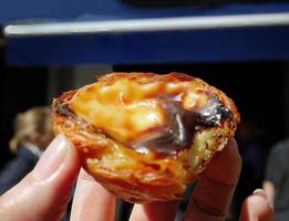 dichtbij omhoog een hand- Holding een traditioneel pasteis de nata traditioneel portugees gebakje keuken ei scherp met romig vulling, vla foto