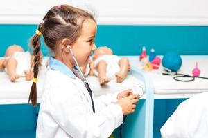 een weinig schattig glimlachen meisje vervelend een dokter uniform met stethoscoop in een ziekenhuis foto