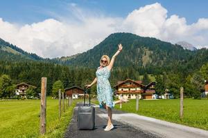 vrouw in de zomer gaat Aan vakantie, Aan vakantie met een koffer Aan de achtergrond van natuur en bergen. de concept van reis, weekend in een mooi plaats in de bergen foto