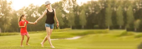 gelukkig familie wandelen Aan gras velden. aanbiddelijk weinig meisje houden haar mam hand- wandelen foto