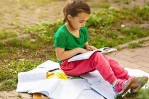 een schattig kind is lezing een boek in de park. foto