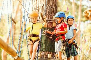 kind in Woud avontuur park. kinderen beklimmen Aan hoog touw pad. beklimming buitenshuis amusement centrum voor kinderen. weinig meisje spelen buitenshuis. school- werf speelplaats met touw manier. foto