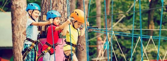 kind in Woud avontuur park. kinderen beklimmen Aan hoog touw pad. behendigheid en beklimming buitenshuis amusement centrum voor kinderen. weinig meisje spelen buitenshuis. school- werf speelplaats met touw manier. foto