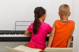 twee weinig kinderen meisje en jongen spelen piano in leven kamer of muziek- school. peuter- kinderen hebben pret met aan het leren naar Speel muziek- instrument. opleiding, vaardigheden concept. foto