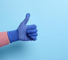 vrouw hand- in blauw werk beschermend handschoen shows de gebaar Leuk vinden Aan een blauw achtergrond foto