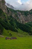 twee boerderijen tussen bergen in de achtergrond een waterval foto