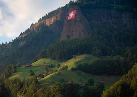 Zwitsers vlag hangende Aan een steil rots gezicht hieronder is een boerderij foto