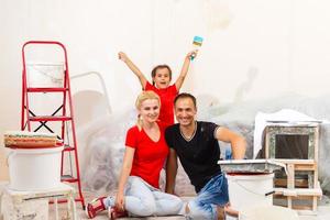 de jong familie doet reparatie Bij huis, een weinig dochter vader en moeder houden platen en verf in handen foto