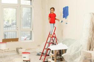 reparatie in de appartement. gelukkig kind meisje verven de muur met blauw verf foto