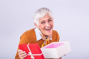 gelukkig volwassen vrouw met een geschenk. geïsoleerd over- achtergrond. mooi elegant senior dame opening haar Kerstmis geschenk. elegant volwassen vrouw Holding een rood geschenk doos foto