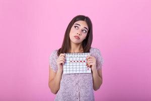 portret van jong vrouw in jurk, Holding vrouw periodes kalender voor controle menstruatie dagen geïsoleerd Aan trending roze achtergrond. medisch gezondheidszorg, gynaecologisch concept. foto