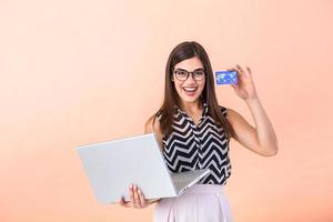 verrast gelukkig brunette vrouw met bril Holding laptop computer terwijl Holding credit kaart en op zoek Bij de camera geïsoleerd Aan achtergrond foto