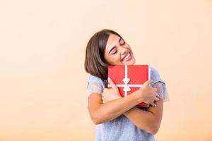 portret van jong lief mooi hoor zoet glamoureus meisje dame, vervelend grijs bovenkant, draag- Kerstmis geschenk doos, benieuwd over verrassing. geïsoleerd over- helder achtergrond foto